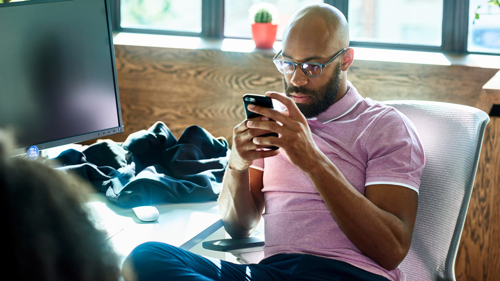 man with beard and glasses texting on phone in office