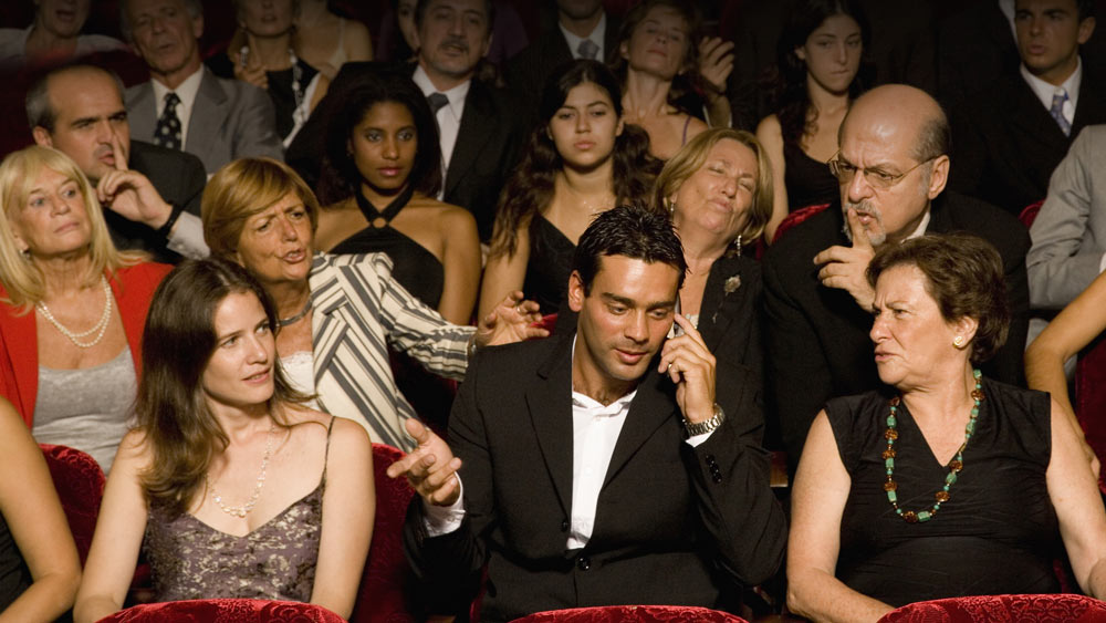 Man speaking on the phone in a theater everyone upset around him