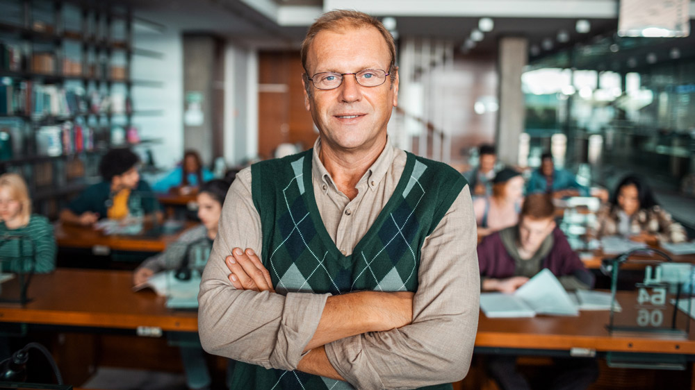 male teacher standing with arms folded in front of his class