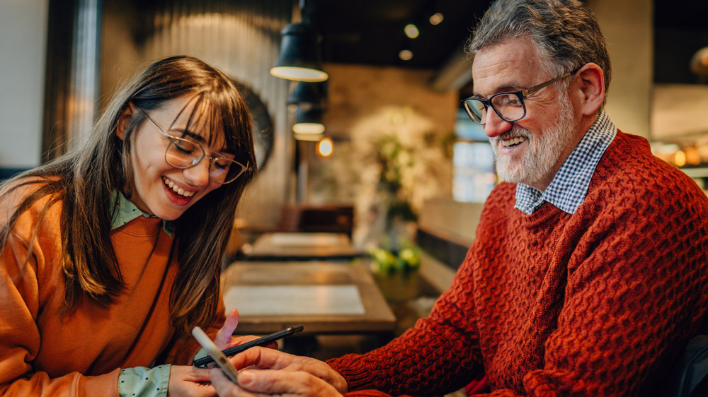 man and teenage girl sitting at cafe talking and laughing