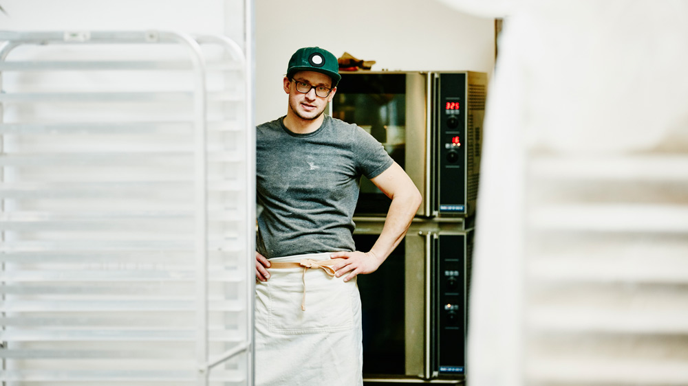 baker standing in kitchen with stains on his shirt