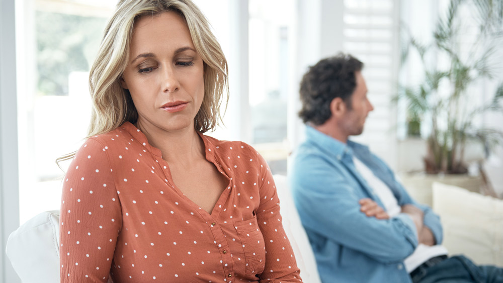 mature couple sitting on opposite ends of couch looking away from each other