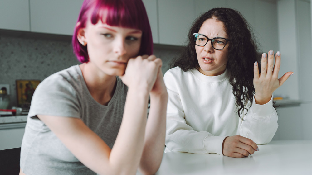 mother and young adult daughter have a serious conversation in the kitchen