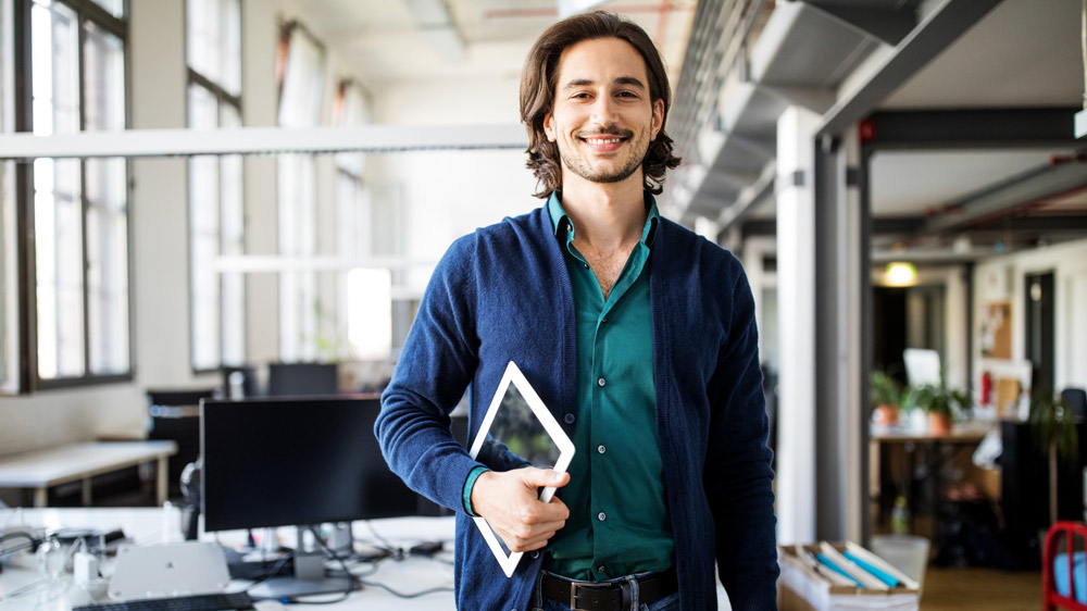 young man in office holding a tablet smiling