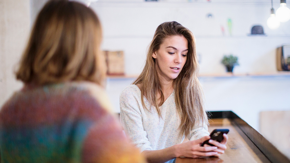 two woman talking, one woman distracted on her smartphone