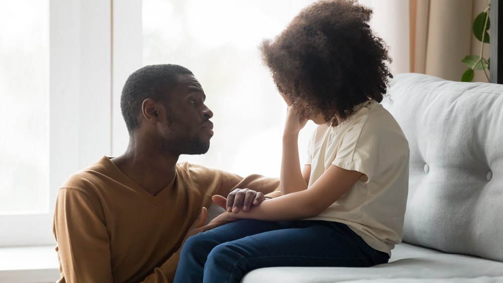 a father kneeling down talking with his upset daughter