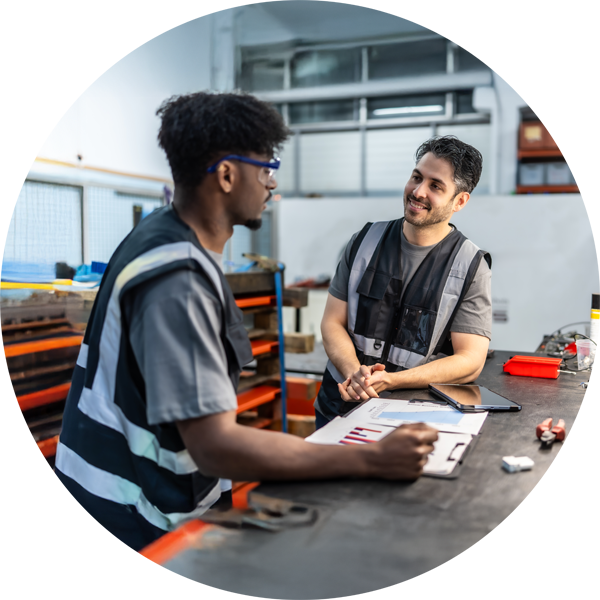 Two men talking at a work bench in a manufacturing warehouse